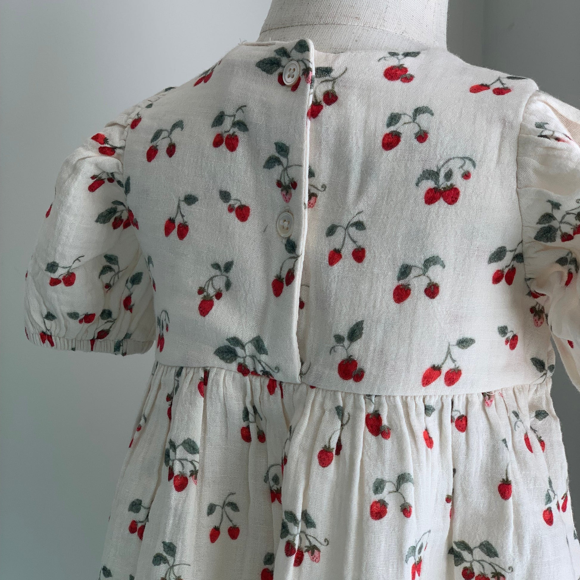 Albertine Dress on mannequin, baby girl organic cotton dress, strawberry print, close up back view  — Willowby, sizes 6–18 months